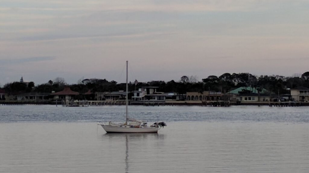 Why I’m Opting Out of Constant Accessibility Small sailboat floating alone on calm water at dusk with shoreline homes in the distance.