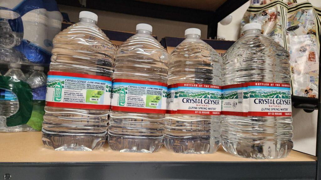Several bottles of drinking water stored on a shelf after being dropped off by family, representing relief from mental load and everyday responsibilities.