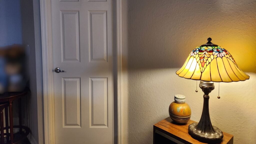 Warm lamp glowing beside a closed door in a quiet home at night, reflecting peace, rest, and choosing solitude without guilt.