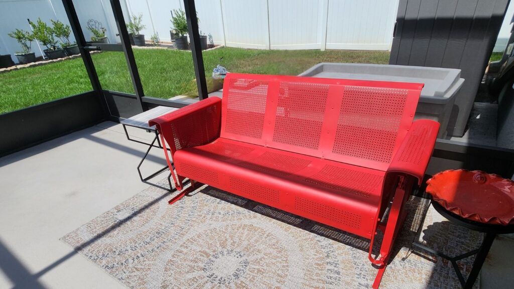Red patio glider in a sunny screened porch, representing choosing rest and making space to slow down.