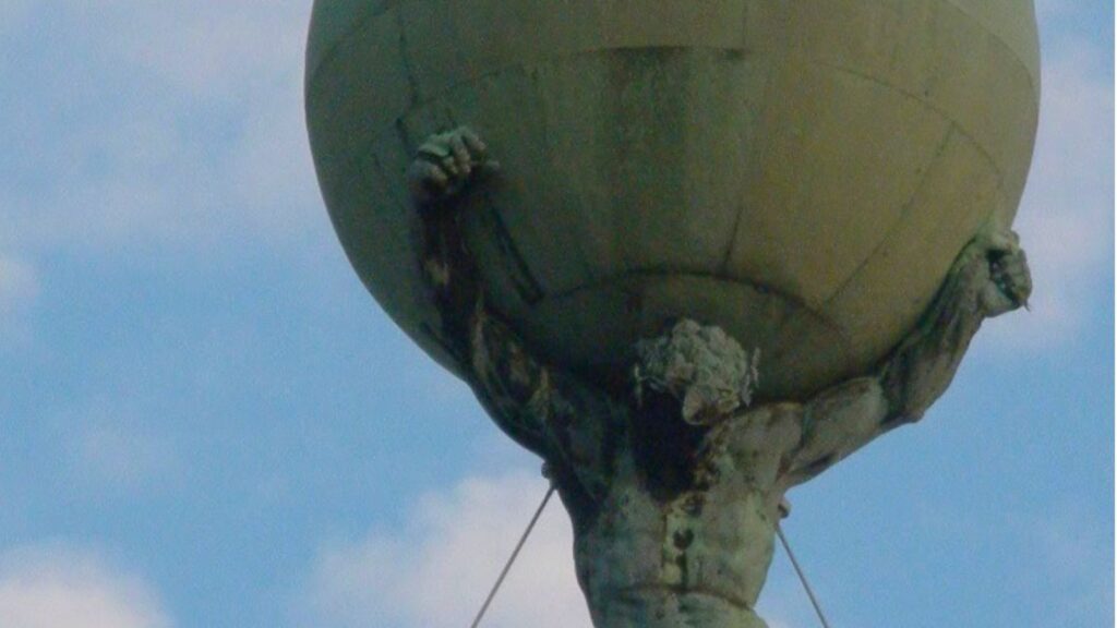 Stone Atlas statue holding a large globe against a blue sky.