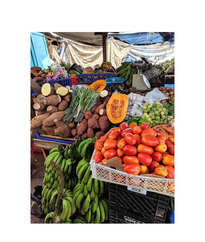 Colorful market display of bananas, tomatoes, root vegetables, and other fresh produce.