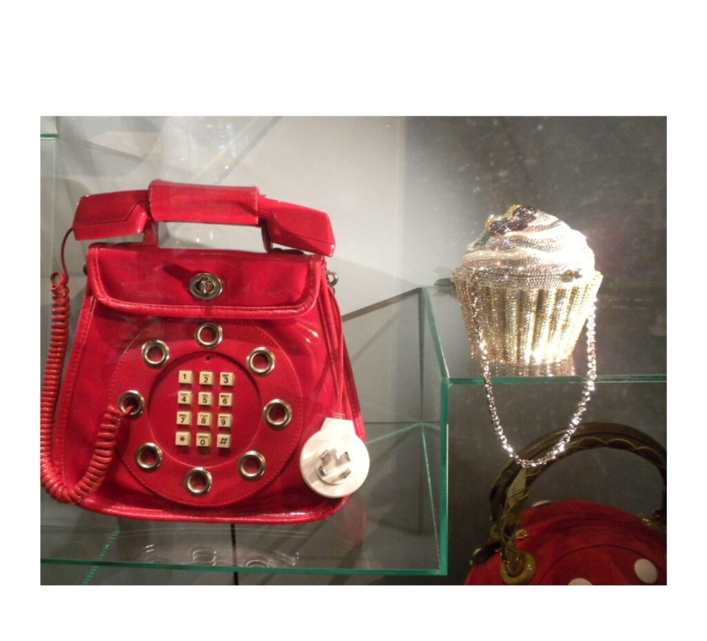 Display featuring a bright red purse shaped like a vintage rotary telephone and a purse shaped like a frosted cupcake.